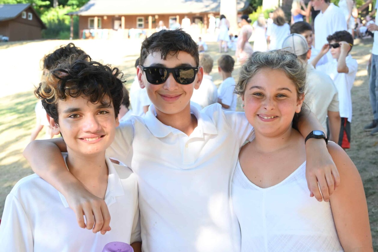 three kids wearing shabbat whites smiling