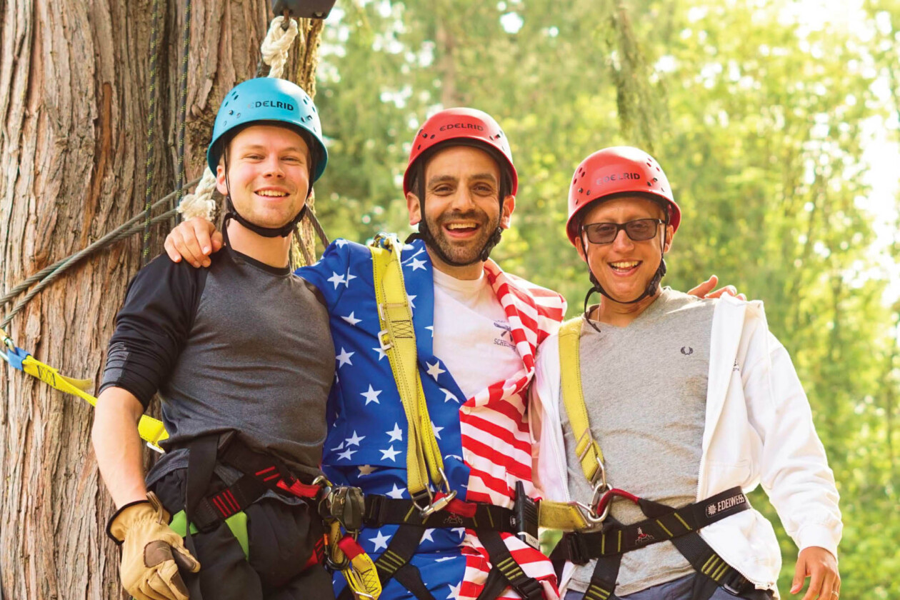 three men in harnesses and helmets next to a tree.