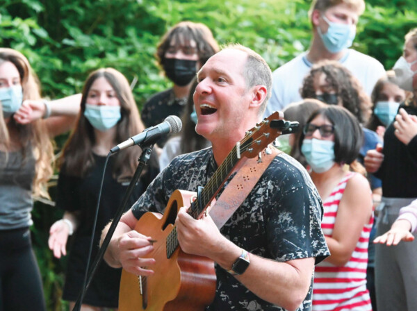 man singing and playing guitar in front of a group of kids.