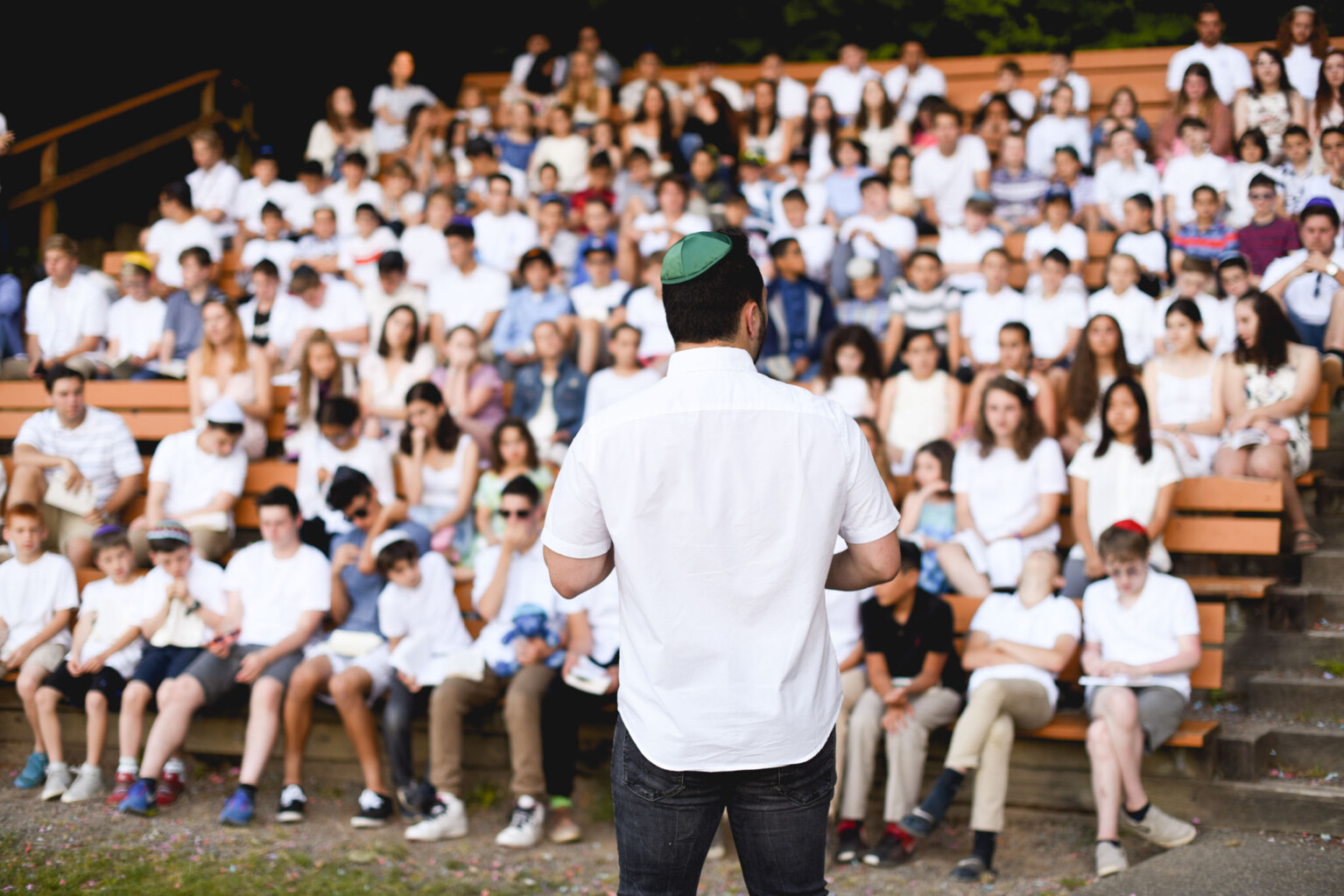 man in white facing an audience of kids in white.