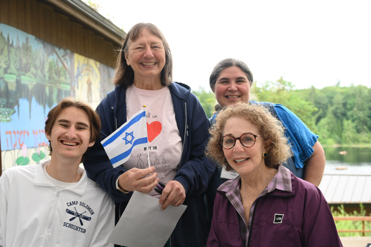 four people outside smiling and holding an israeli flag.