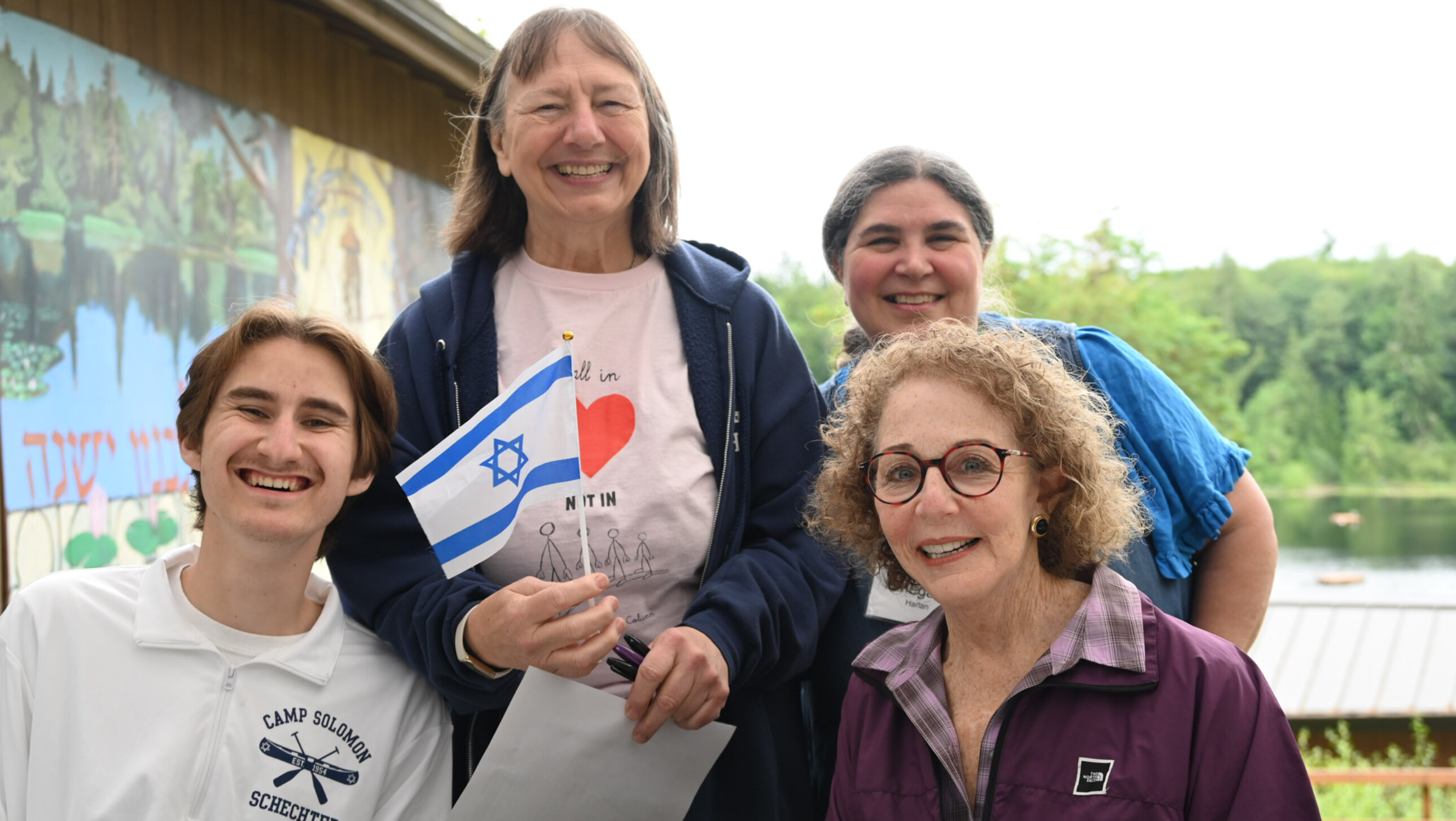 four people outside smiling and holding an israeli flag.